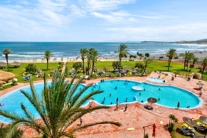Widok z góry na basen, plażę i ocean w słoneczny dzień.
