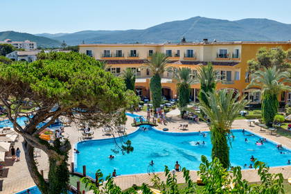 Hotel z basenem, palmami i górami w tle.