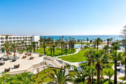 Hotel z palmami i trawnikiem, w tle morze.