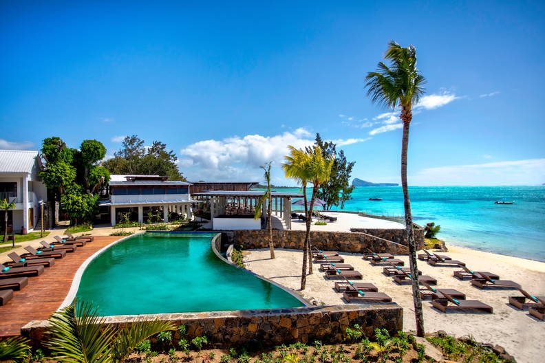 Turkusowy basen z palmami i leżakami przy plaży.