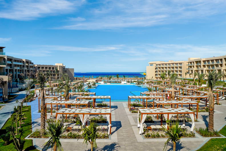 Ośrodek wypoczynkowy z basenem, palmami i pawilonami.