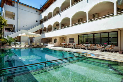 Basen hotelowy z leżakami, parasolami i stolikami z krzesłami.