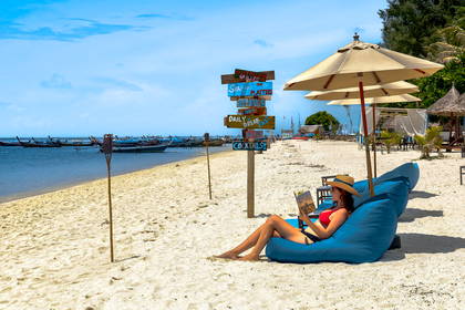 Kobieta czyta książkę, leżąc na leżaku na plaży.