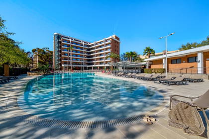 Hotel z basenem i leżakami w słoneczny dzień.