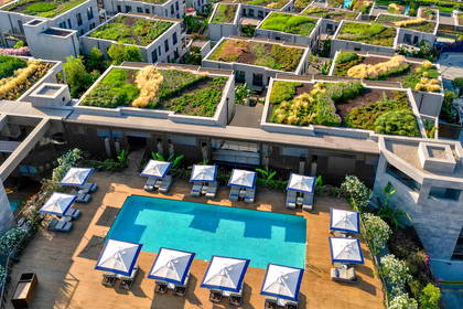 Luksusowy hotel z basenem i zielonymi dachami widziany z góry, w tle morze.