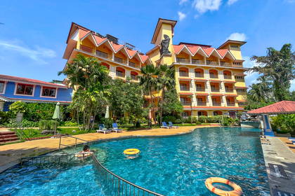 Żółty hotel z czerwonym dachem nad basenem w słoneczny dzień.