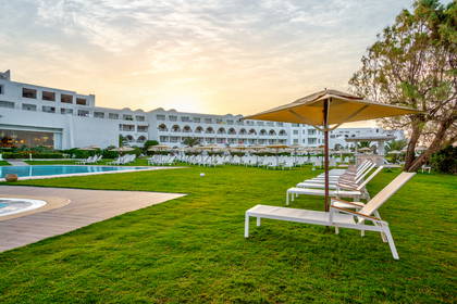 Hotel z basenem, trawnikiem, leżakami i parasolami.