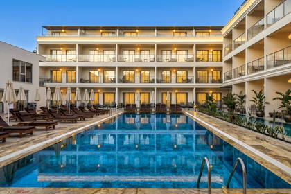 Basen hotelowy otoczony leżakami na tle oświetlonego budynku hotelowego o zmierzchu.