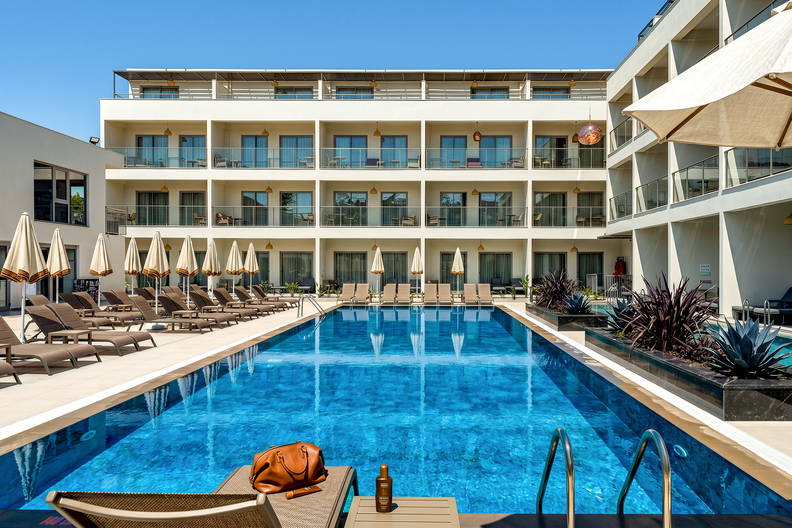 Nowoczesny hotel z długim basenem otoczonym rzędami leżaków i parasoli.