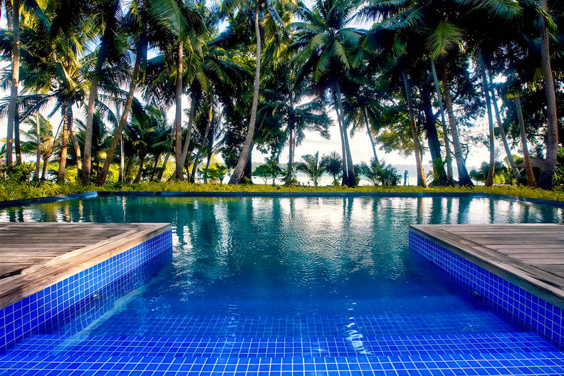 Basen z błękitną wodą otoczony palmami.