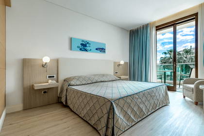 Pokój hotelowy z łóżkiem, balkonem i widokiem na palmy.