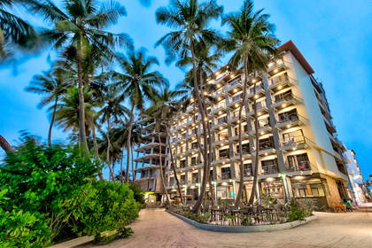 Hotel z balkonami otoczony palmami.