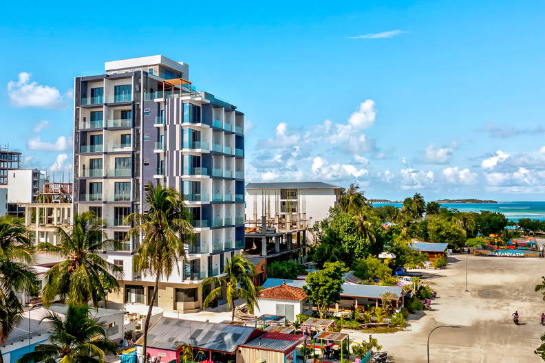 Budynek z balkonami, palmy i błękitne niebo w tle.