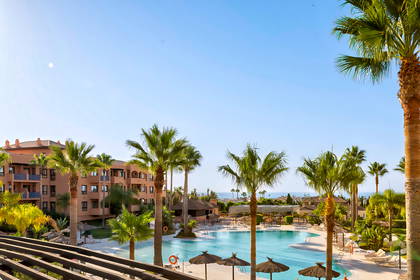 Hotelowy basen otoczony palmami i budynkami.