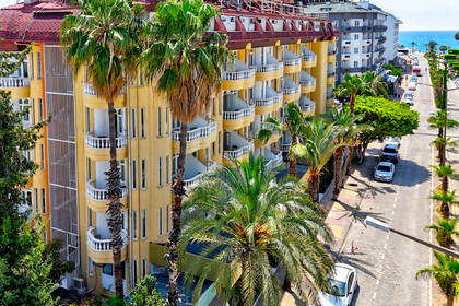 Żółty hotel z balkonami otoczony palmami.