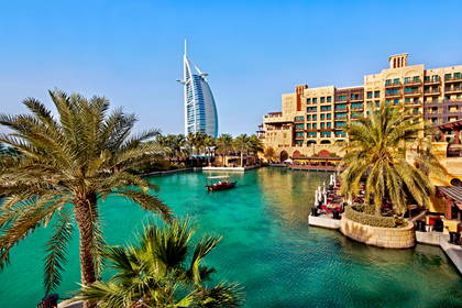 Burj Al Arab widziany z kanału w Dubaju. W tle palmy i zabudowa miasta.