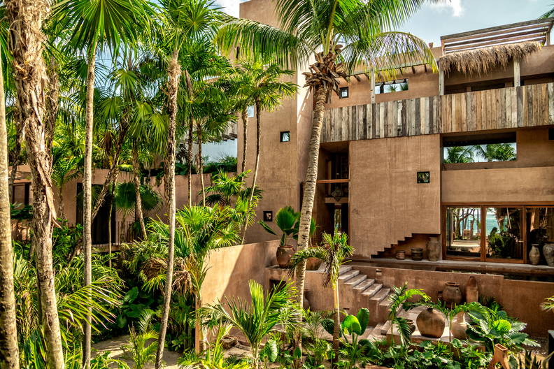 Budynek z beżową fasadą otoczony tropikalną roślinnością.