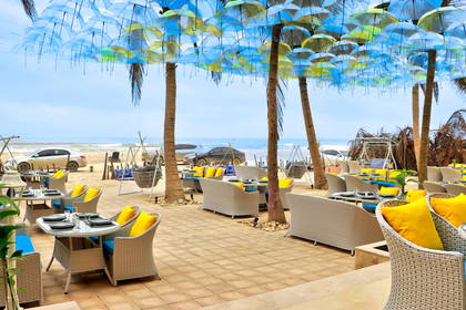 Restauracja na plaży z parasolami zawieszonymi na drzewach.