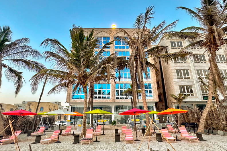 Plaża z palmami i leżakami. W tle budynki.