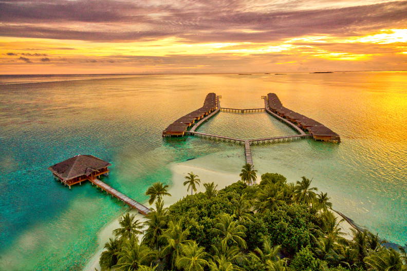 Tropikalna wyspa z domkami na wodzie o zachodzie słońca, widok z lotu ptaka.