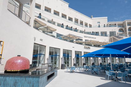 Restauracja Culina Mediterranean z piecem do pizzy na zewnątrz i niebieskimi parasolami.