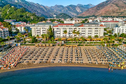 Plaża z hotelami widziana z lotu ptaka, w tle góry.