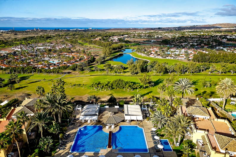 Widok z góry na basen, palmy, pole golfowe i budynki.