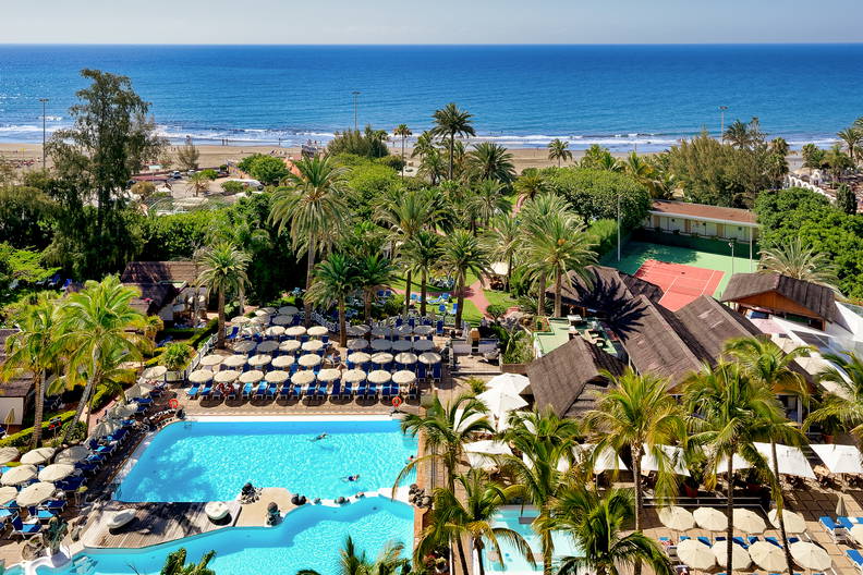Kurort z basenami i palmami widziany z góry, w tle plaża.