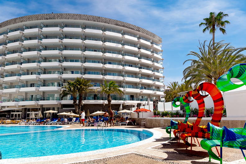 Hotel z basenem i palmami w słoneczny dzień.