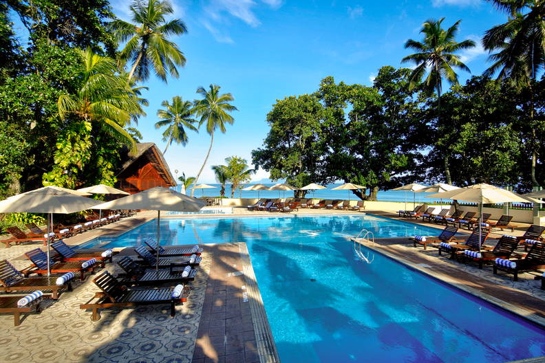 Basen w tropikalnym kurorcie. Wokół leżaki i palmy.