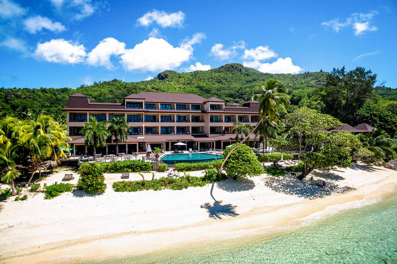 Hotel z basenem przy plaży, wśród tropikalnej roślinności.