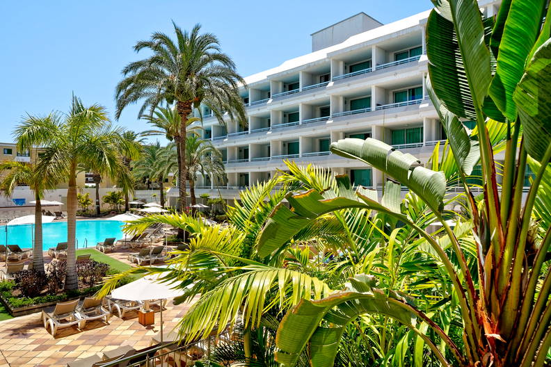 Hotel z basenem, leżakami i palmami.
