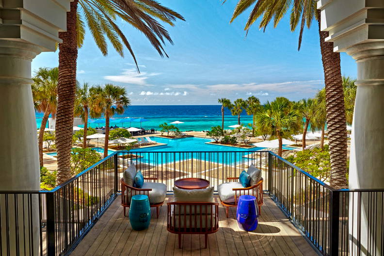 Widok z balkonu na ocean, palmy i basen.