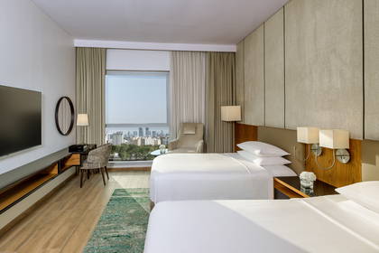 Pokój hotelowy z dwoma łóżkami, biurkiem i widokiem na miasto.