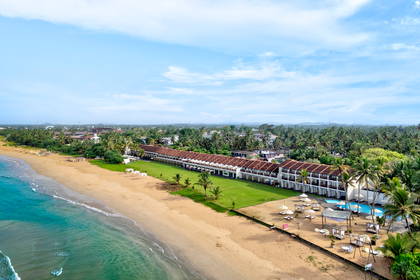 Hotel przy plaży z lotu ptaka. Widoczne palmy i błękitna woda.