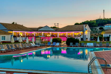 Hotel z basenem, leżakami i restauracją podświetloną na różowo.