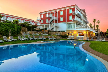 Hotel z basenem i leżakami na trawniku w świetle zachodzącego słońca.