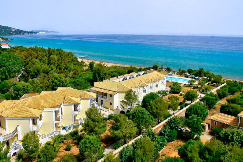 Widok z góry na nadmorski kurort. Widać żółte budynki i basen.