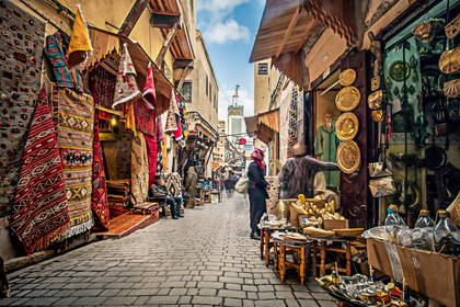 Ulica w Marrakeszu z kramami i przechodzącymi ludźmi.