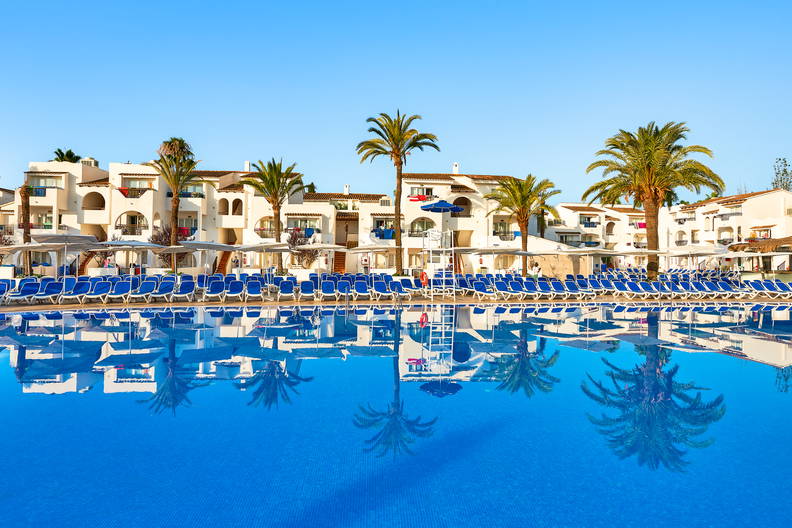 Hotel z basenem, leżakami i palmami.