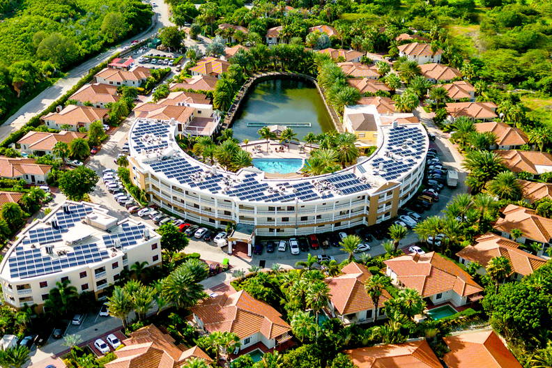 Kompleks budynków z panelami słonecznymi, basenem i stawem, widok z lotu ptaka.