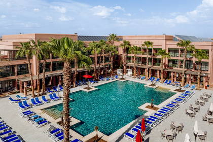 Hotel z basenem otoczonym palmami i leżakami, widok z góry.