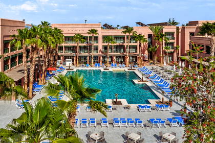 Hotel z basenem, leżakami i palmami.