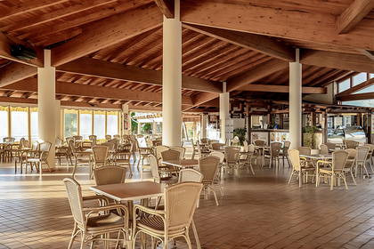 Restauracja z drewnianym stropem, kolumnami i rattanowymi meblami.