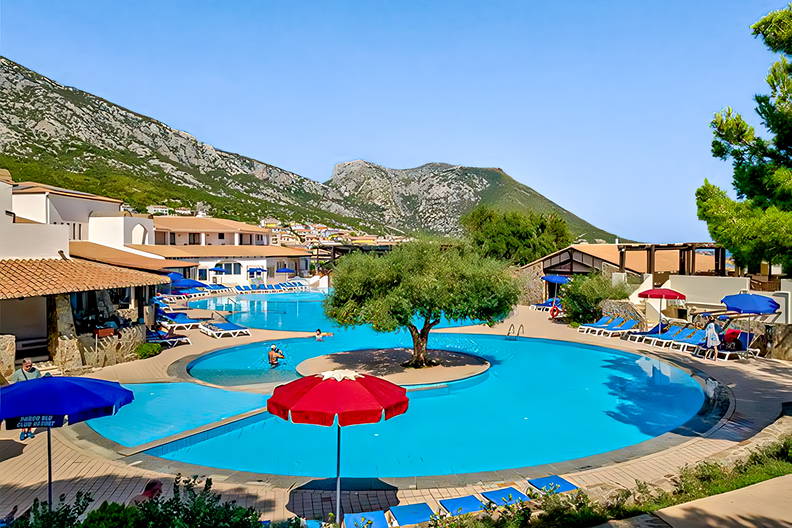 Basen z drzewem pośrodku, leżakami i widokiem na góry.