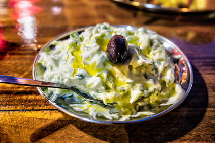 Tzatziki z oliwką i łyżką na srebrnym talerzu.