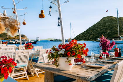 Restauracja na plaży z widokiem na morze, stoliki udekorowane kwiatami.