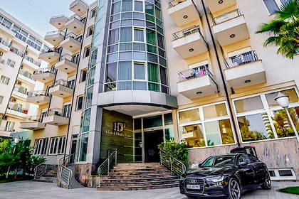 Fasada hotelu z balkonami i szklaną wieżą. Przed wejściem czarne Audi.