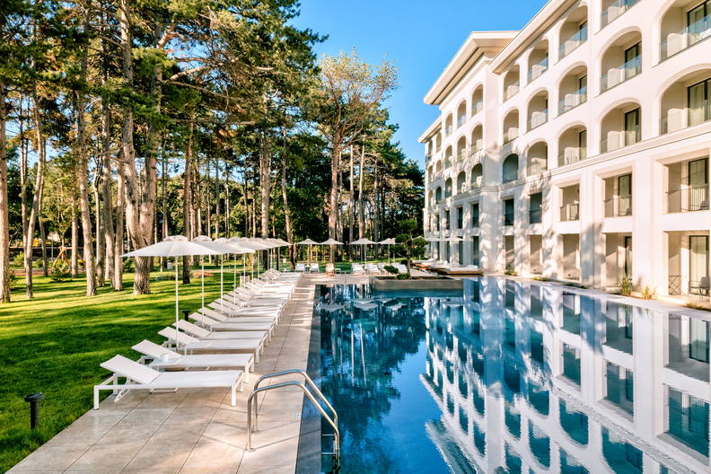 Hotel z basenem i leżakami, w tle las.