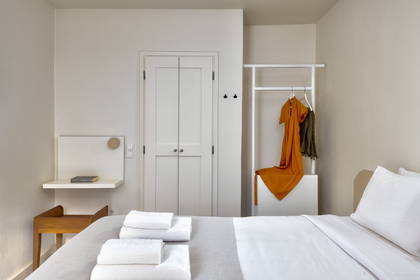 Jasny pokój hotelowy z łóżkiem, ręcznikami i ubraniami.